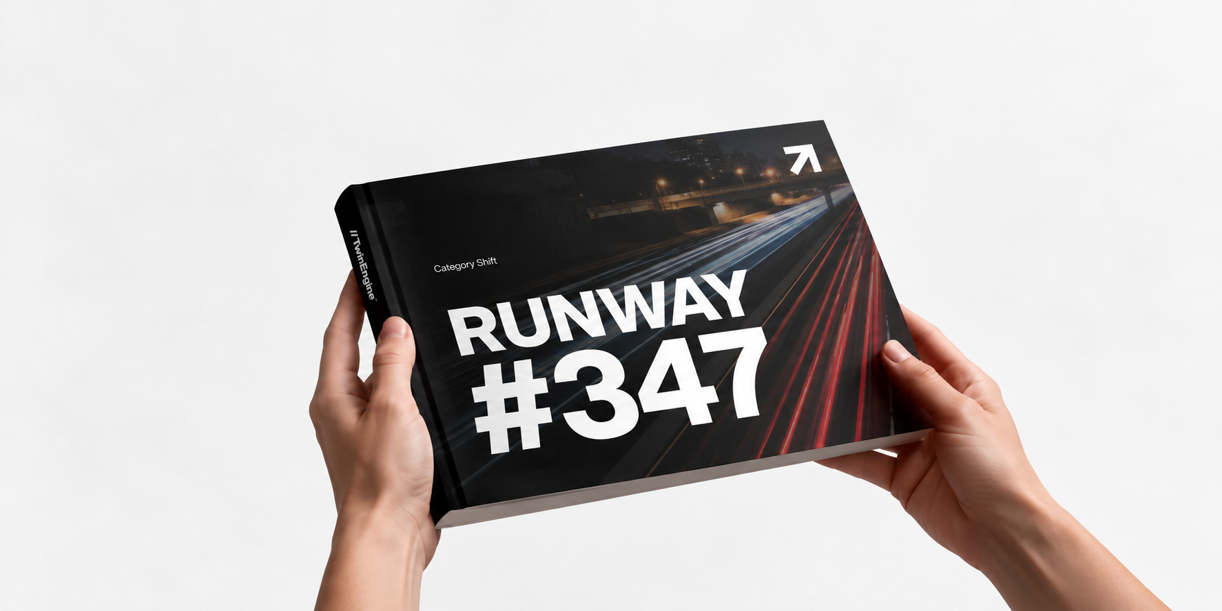 Two hands holding the Runway booklet, its black cover showing a night highway with light trails and the words RUNWAY #347, with the TwinEngine name along the spine